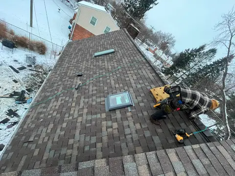 Roofer installing shingles on a snowy residential roof